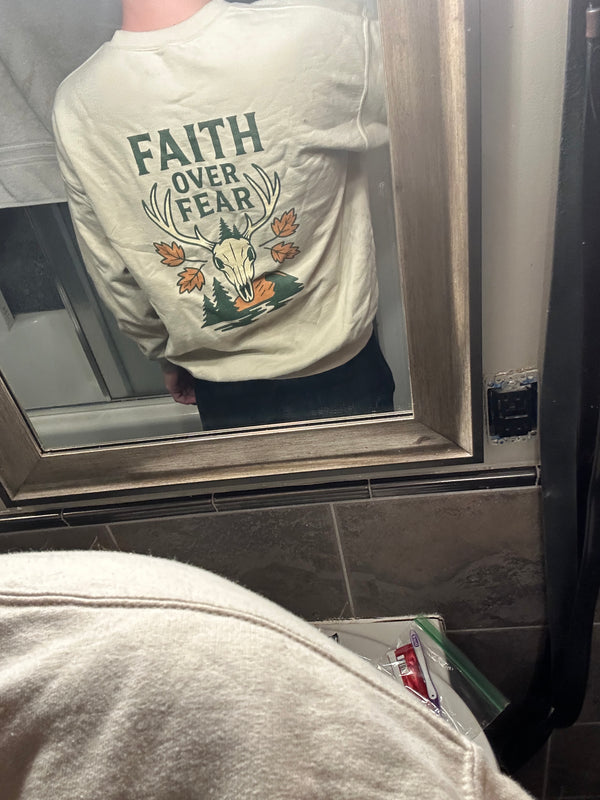 Person taking a mirror photo wearing the Rack & River Outdoors ‘Faith Over Fear’ deer skull graphic sweatshirt.