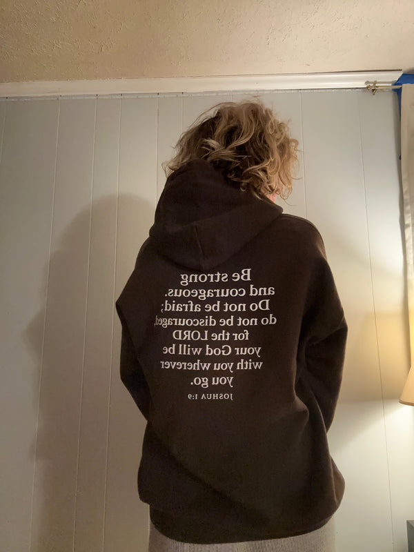 Person wearing the Rack & River Outdoors Joshua 1:9 Scripture hoodie, shown from the back with the Bible verse graphic.